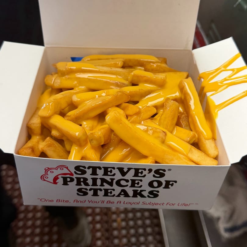 Steve's Prince of Steaks cheese fries in a white box with cheese drizzled on the side.