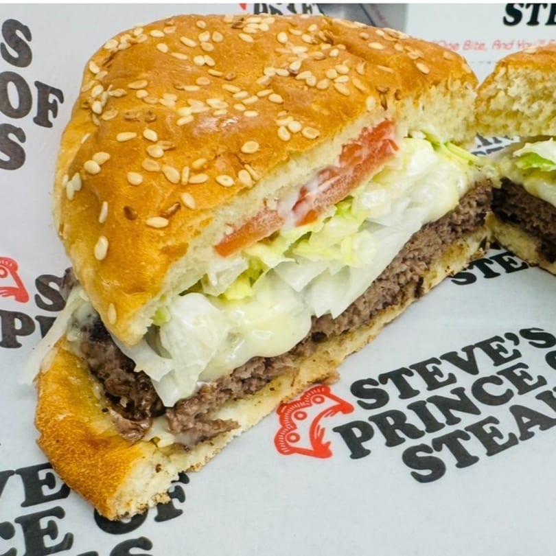 A sliced cheeseburger with lettuce, tomato, and melted cheese on a sesame seed bun.