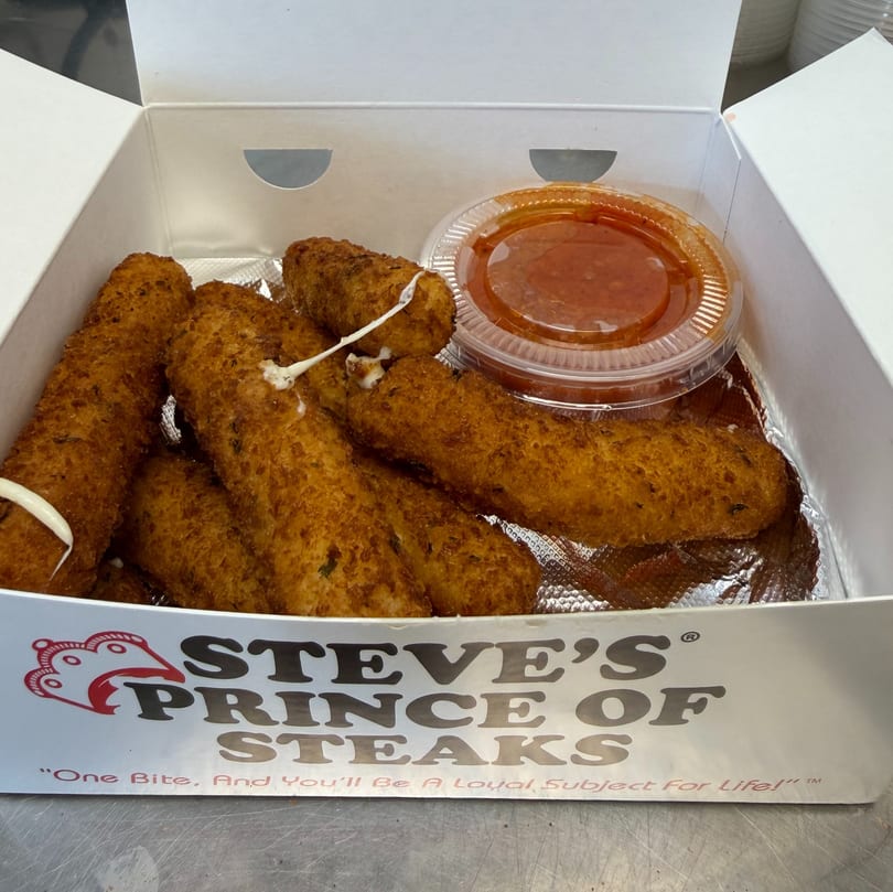 Mozzarella sticks with marinara sauce in a Steve's Prince of Steaks takeout box.