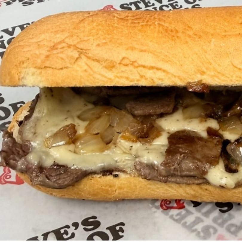 A close-up of a cheesesteak sandwich with melted cheese, steak, and caramelized onions on a hoagie roll.