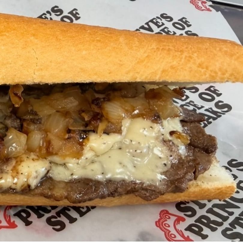 A close-up of a Philly cheesesteak sandwich with melted cheese and caramelized onions.