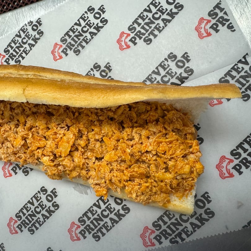 A Steve's Prince of Steaks cheesesteak, filled with finely chopped steak, on branded wax paper.