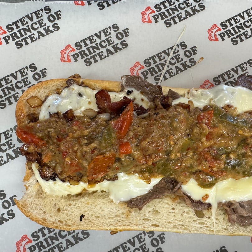 A Steve's Prince of Steaks cheesesteak with melted cheese, peppers, and onions on branded paper.