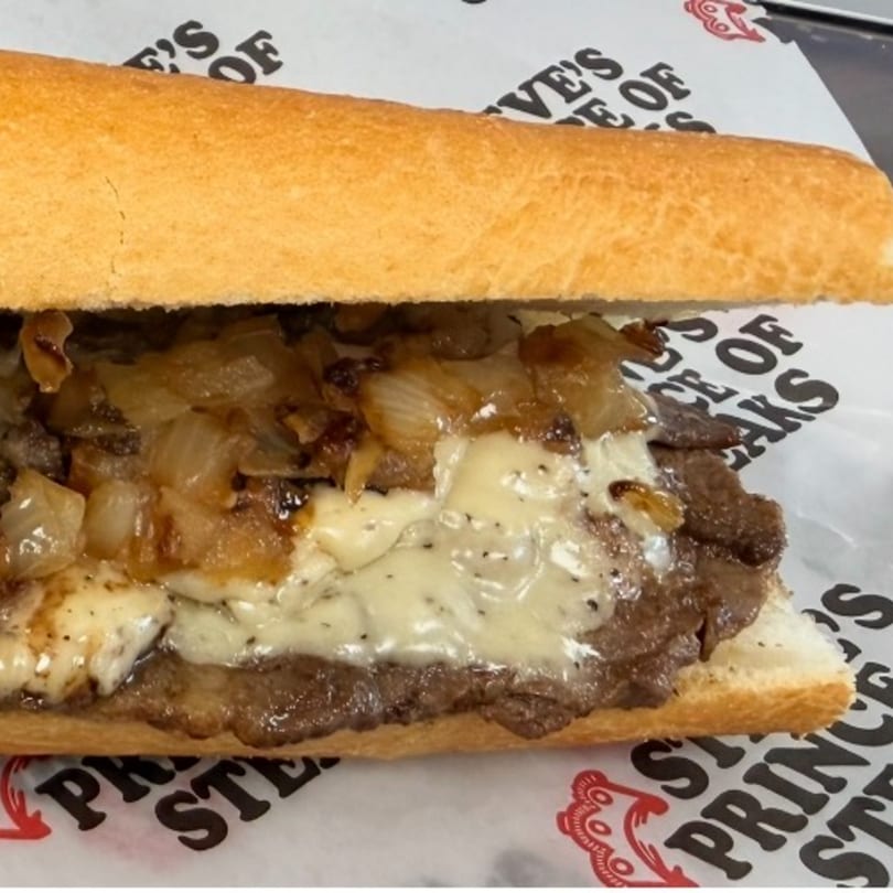 A close-up of a cheesesteak sandwich with melted cheese and caramelized onions on a roll.