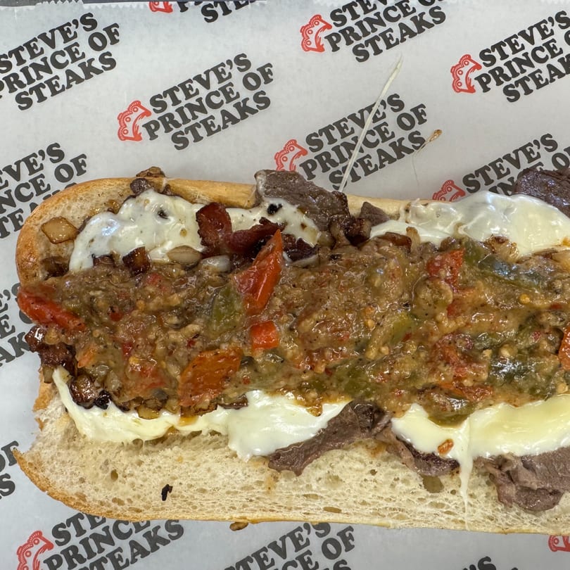 A close-up of a Steve's Prince of Steaks cheesesteak with melted cheese, steak, and peppers.