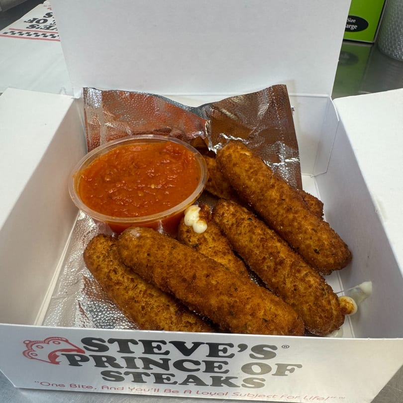 Steve's Prince of Steaks mozzarella sticks with marinara sauce in a white takeout box.