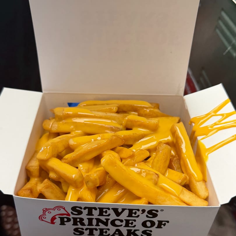 A white cardboard container from Steve's Prince of Steaks filled with golden french fries covered in melted cheese.