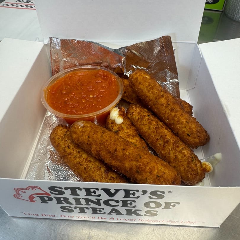 Golden-brown mozzarella sticks with marinara sauce in a Steve's Prince of Steaks branded box.